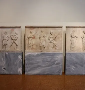 Mantineia Base relief slabs showing classical figures, including musicians and seated or standing characters, displayed side by side.