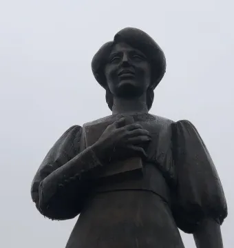 Bronze statue of Zabel Yessayan holding a book against her chest and looking upward.