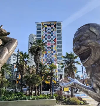 A-maze-ing Laughter bronze statues in a public square with a high-rise building and palm trees behind them.