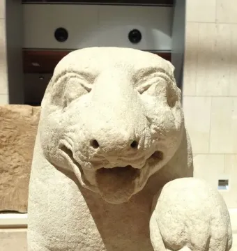 Close-up of the Bear of Porcuna showing a carved animal head and upper torso with an open mouth and closed eyes, with a smaller human head beside it.