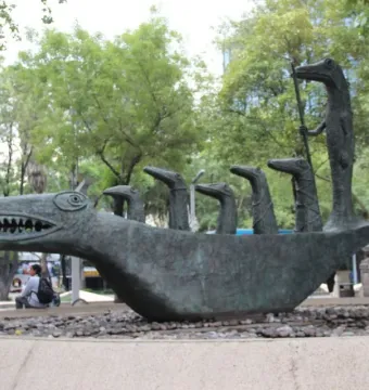 How Doth the Little Crocodile sculpture in a stone basin with pebble ground and trees behind it