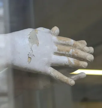 Clasped hands from the Mary Magdalene penitente sculpture, with peeling light-colored surface exposing darker material underneath.