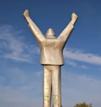 Monument to Stjepan Filipović, a silver-toned faceted statue with raised clenched fists on a graffiti-marked base against the sky.