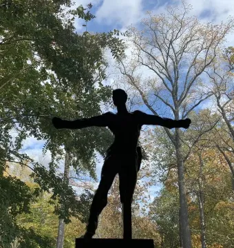 Standing Mercury by Auguste Rodin silhouetted against a bright blue sky with trees behind it.