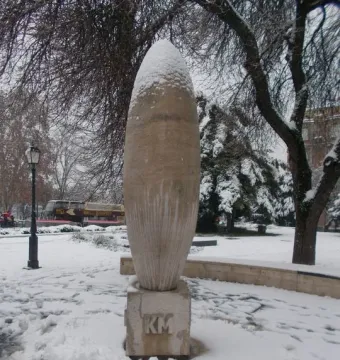 Zero Kilometre Stone topped with snow in a snowy park, with bare trees in the background.