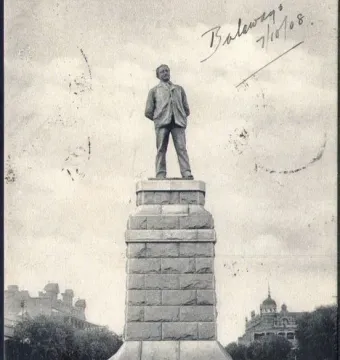 Statue of Cecil Rhodes on a tall stone pedestal in an outdoor paved area.