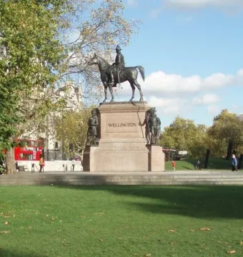 The Duke of Wellington equestrian statue on a tall stone pedestal in an urban plaza, with people and traffic nearby.