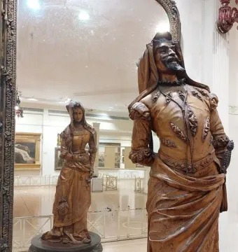 Mephistopheles and Margaretta wooden sculpture with a bearded man in ornate clothing and a reflected woman in a hooded dress