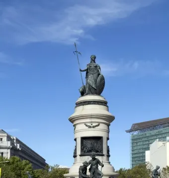 Pioneer Monument in San Francisco, with a bronze crowned female figure atop a tall stone column, sculptural groups at the base, and a fenced foreground.