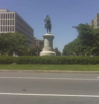Winfield Scott equestrian statue on a tall pedestal in a grassy median with trees and city buildings behind it.