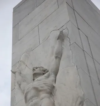 Close-up of the Alamo Cenotaph showing a stone relief of a muscular man with raised arms.