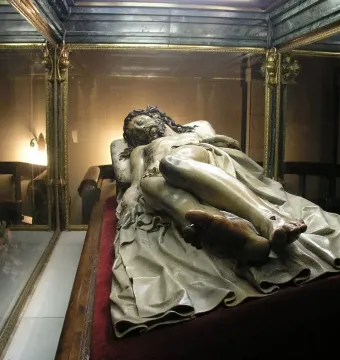Cristo Yacente reclining wooden sculpture displayed in a glass case