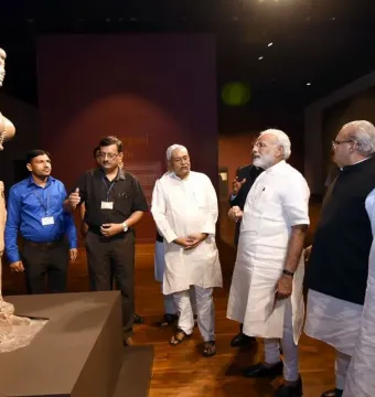 Didarganj Yakshi statue displayed on a dark pedestal in a museum, with part of the left arm missing and visitors standing nearby.