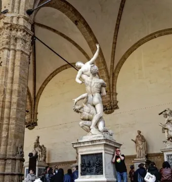 Rape of the Sabine Women marble sculpture beneath a stone loggia, with visitors seated nearby