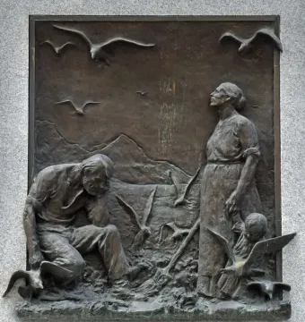Bronze relief on the Seagull Monument showing a kneeling man and standing woman surrounded by seagulls, with mountains in the background.
