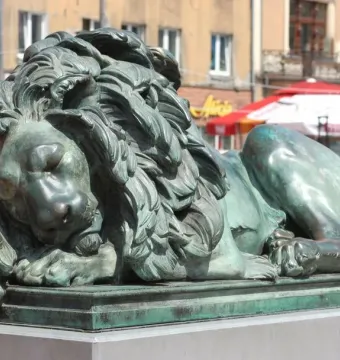Sleeping Lion bronze sculpture with a green patina, shown lying with its head resting on its front paws.