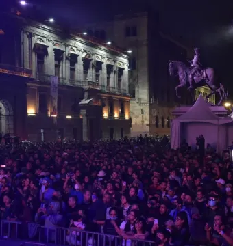 El Caballito equestrian statue lit with purple stage lights at night, with a crowd and event tents in front of it.