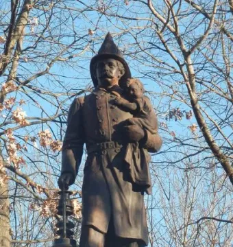 Firemen\'s Monument showing a bronze rescue worker holding a child and a lantern on a stone pedestal.