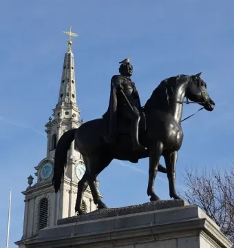 Equestrian statue of George IV on a stone pedestal, with a church steeple and clock tower behind it.