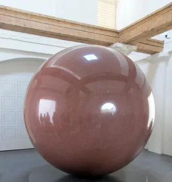 Large Red Sphere on a dark stepped pedestal in a bright room with wooden beams overhead.