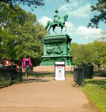 Major General John A. Logan equestrian statue on an ornate pedestal in a park, with a notice sign nearby.