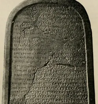 The Mesha Stele, a dark ancient stone slab with a rounded top covered in carved inscriptions and visible cracks.