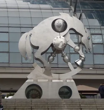 Rolling Horse sculpture in front of a modern glass building, mounted on a concrete pedestal with round openings.