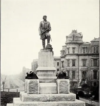 The Admiral David G. Farragut statue stands on a tall stone pedestal beside two small mortars, with a domed building in the background.