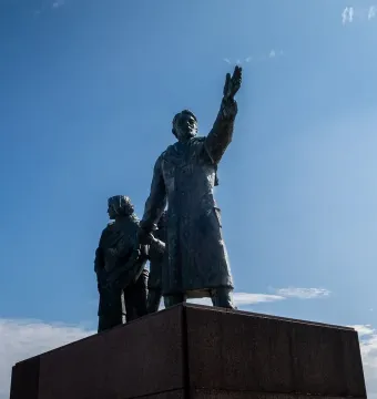 Auswandererdenkmal sculpture with a figure waving from a group of dark metal figures on a tall stone pedestal.