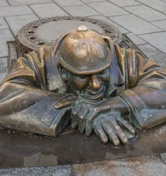 Čumil bronze statue of a man emerging from a manhole in a stone-paved street