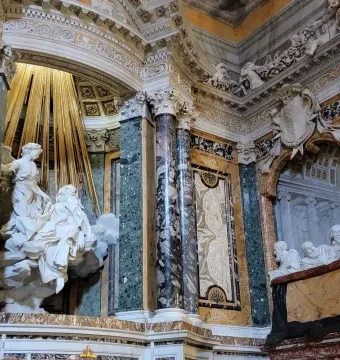 Ecstasy of Saint Teresa marble sculpture with an angel above a reclining figure under golden rays in an ornate niche.