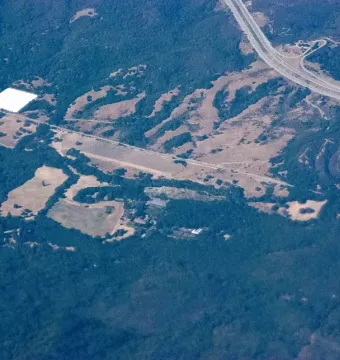 Aerial view of the Pulgas Water Temple surrounded by forest and open land near a highway.