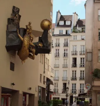 The Defender of Time sculpture with a bronze dragon-like creature, seated figure, and gold clock orb on a building facade.