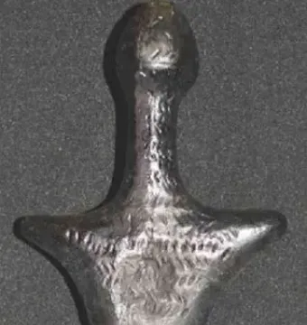 Back view of the Venus of Langenzersdorf sculpture, a dark stylized female figurine with broad shoulders and rounded hips.