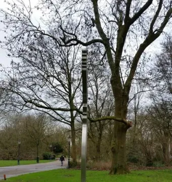 De Schreeuw, a tall metallic sculpture standing on grass in a park beneath an overcast sky.