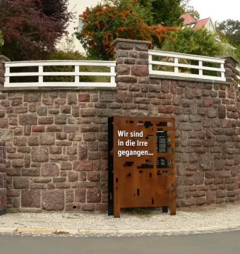Dejudaization Institute memorial sign beside a curved stone wall and sidewalk in Eisenach.