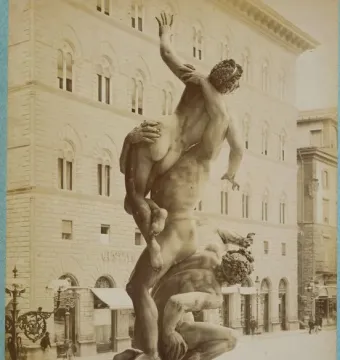 Giambologna’s Rape of the Sabine Women sculpture in a public square, with three intertwined figures against a building with arched windows.
