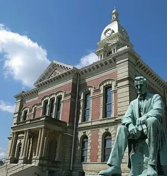 The Lincoln Monument, a seated greenish metal statue in front of a brick courthouse with a clock tower.