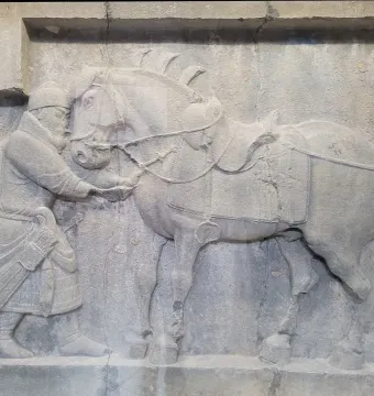 Limestone relief from the Six Steeds of Zhao Mausoleum showing a uniformed figure beside a saddled horse.