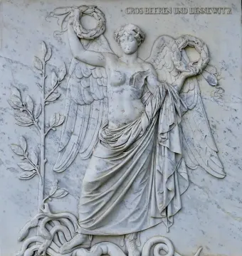 Winged female figure in relief on the Bülow Monument, holding circular wreaths with the inscription \