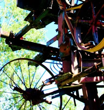 Close-up of Heureka showing rusted gears, wheels, and beams with a yellow belt against green trees and blue sky.