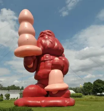 A massive inflatable Santa Claus stands on a grassy lawn holding a large pink object, with another pink object near its left leg.