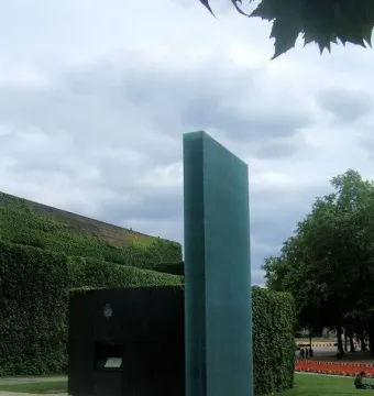 National Police Memorial in London, showing a tall dark teal monolith rising from a rectangular pool beside a smaller dark block and landscaped lawns.