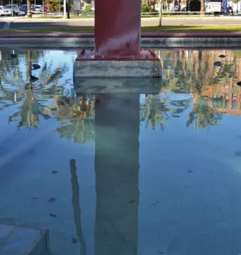 A shallow pool reflecting palm trees and buildings with a reddish-brown Pink Panther sculpture rising from the center.