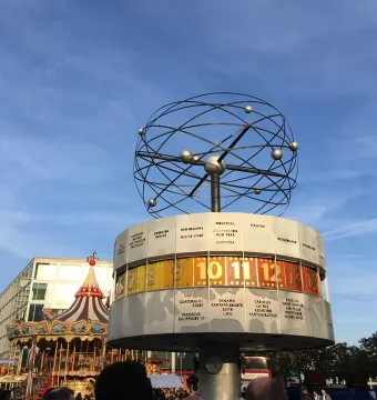 World Clock with an open metal globe on top and city names around the base, with a carousel in the background.