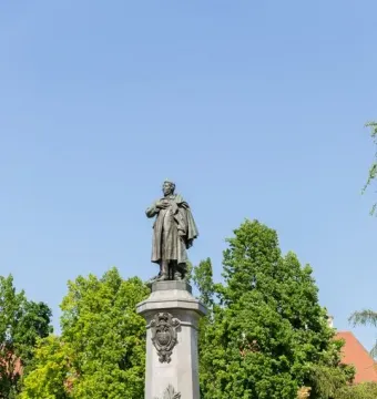 Adam Mickiewicz Monument: a bronze statue of a man in a cloak standing on a tall stone pedestal, with a floral wreath at the base.