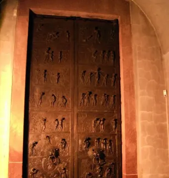 Bernward Doors with bronze relief panels and animal-head door knockers in a stone archway.