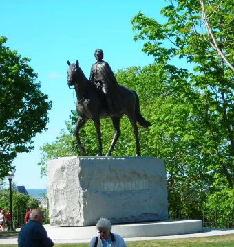 Elizabeth II Equestrian Statue on a stone pedestal with trees and a blue sky behind it