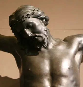 Bronze sculpture of the crucified Christ with bowed head, closed eyes, and outstretched arms.