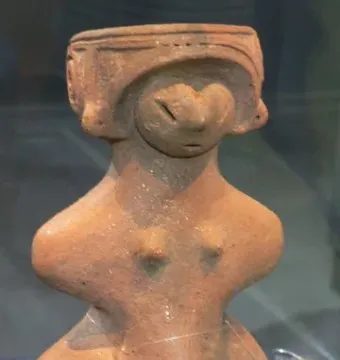 Jōmon Venus clay figurine with a stylized head, prominent breasts, and a rounded lower body on a dark base.
